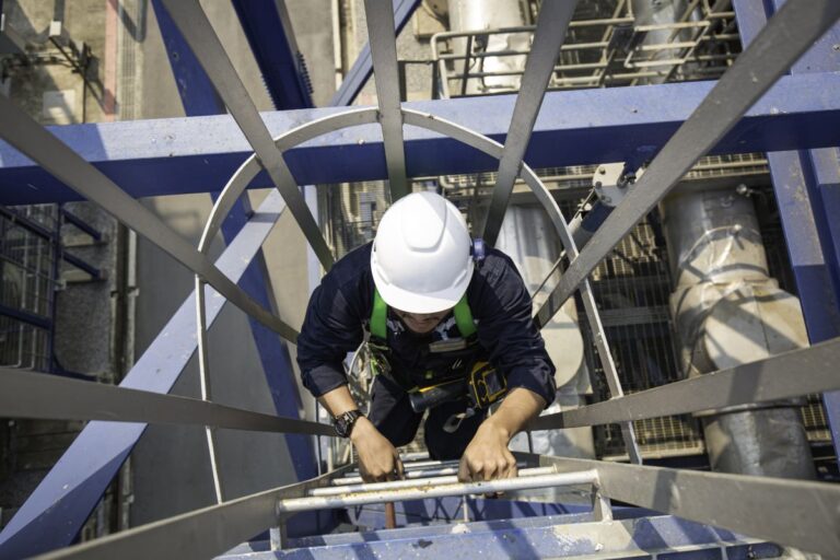 Obrero subiendo escaleras con protección anticaída en instalación industrial
