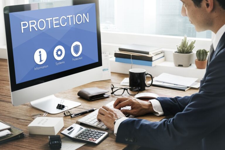 Hombre en oficina consultando ordenador. En la pantalla aparece la palabra "protection" y varios iconos informáticos